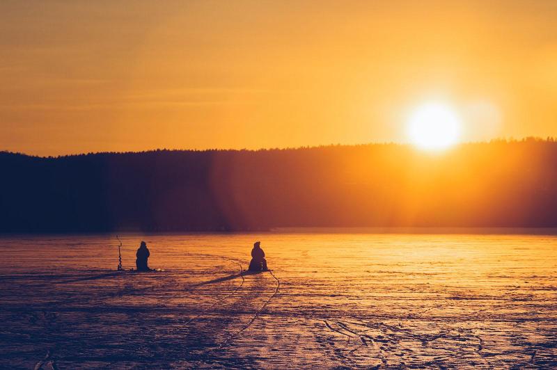 Two people silhouetted by the son while ice fishing 