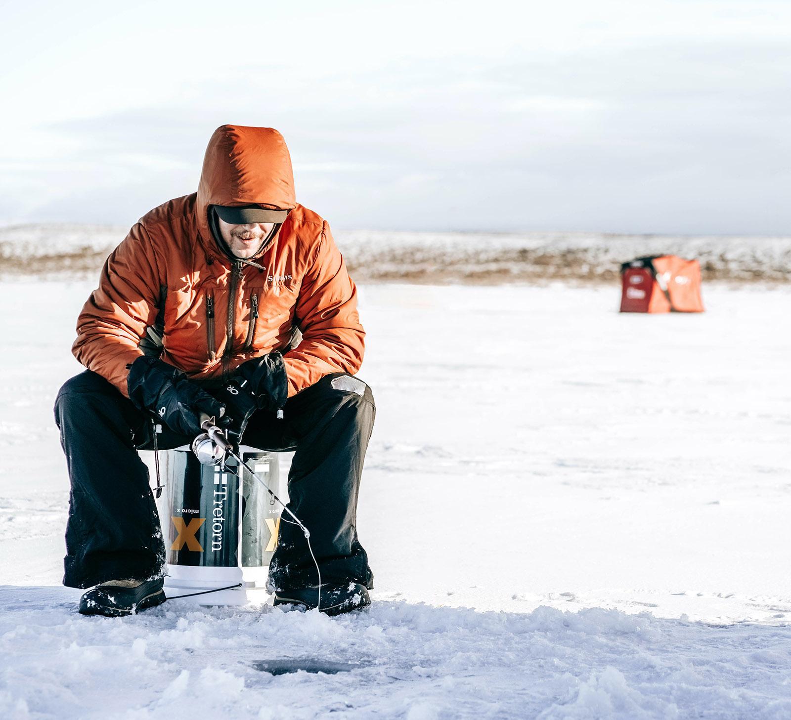 Man sitting on bucket with fishing rod cast into ice fishing hole