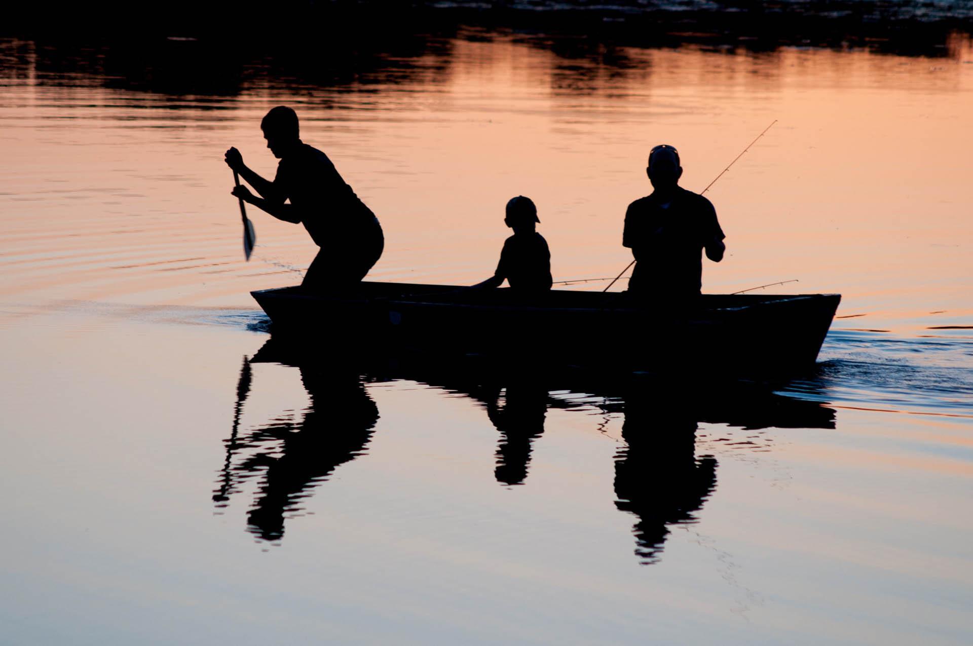 Three people fishing from a boat. 