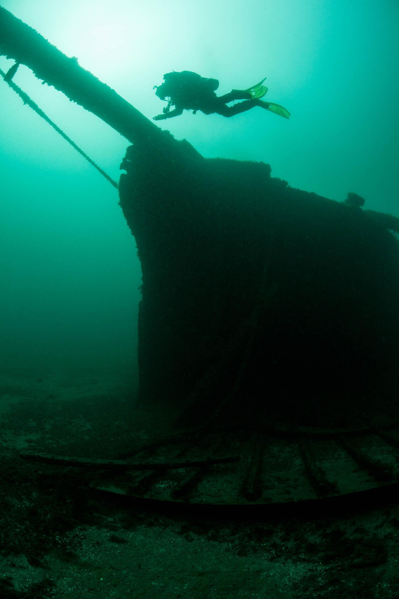 A scuba diver explores an old wooden shipwreck.