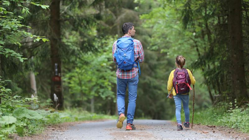 a father and daughter hiking a wide path in woods