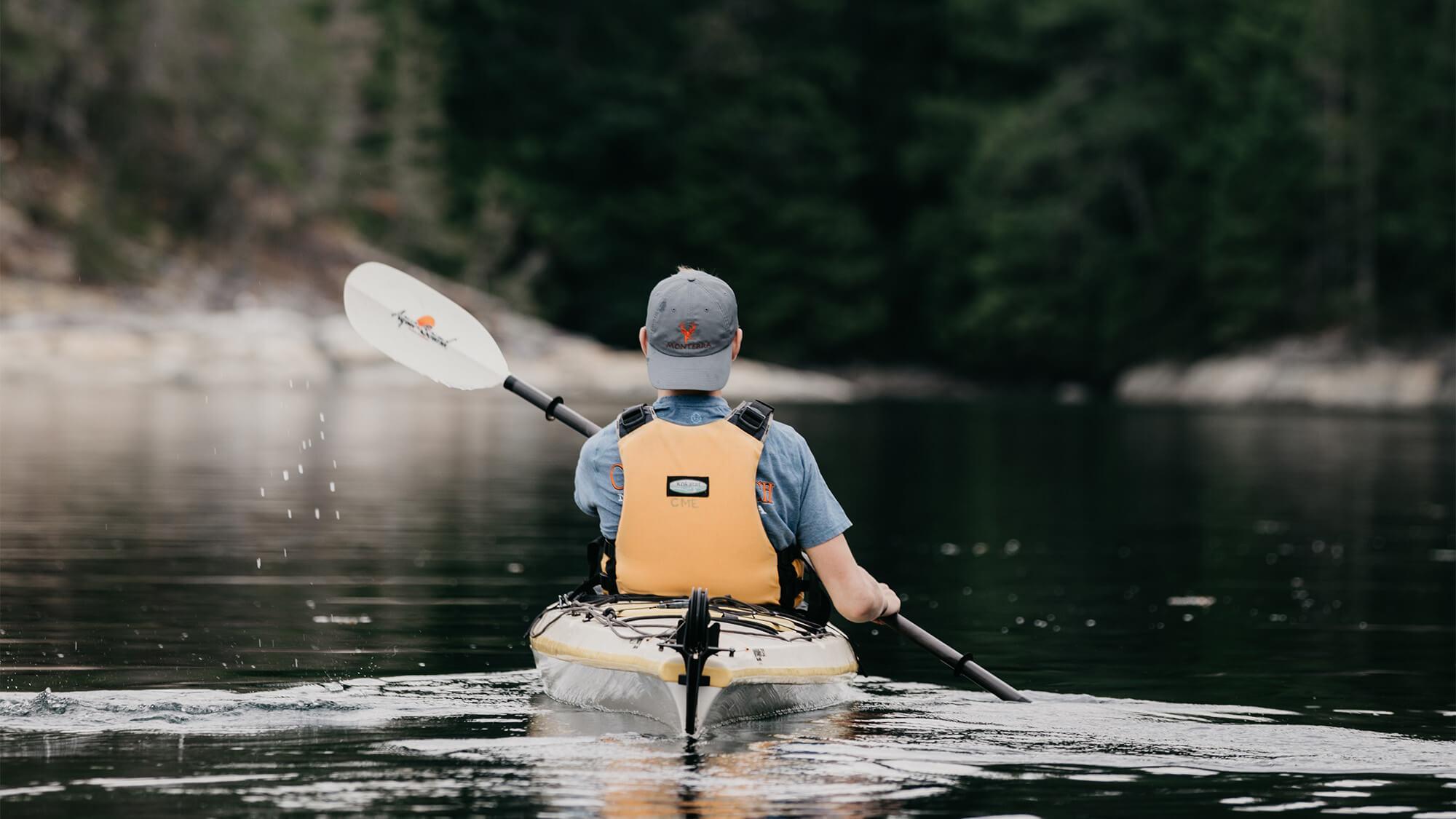 man kayaking towards a tree lined shore